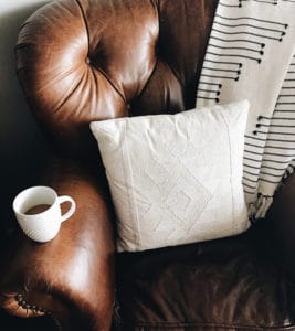 A chair with pillow and coffee mug.